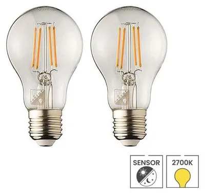 Two clear glass LED light bulbs with filament elements are shown side-by-side against a white background. Below the bulbs are two icons, one indicating a sensor and the other a color temperature.