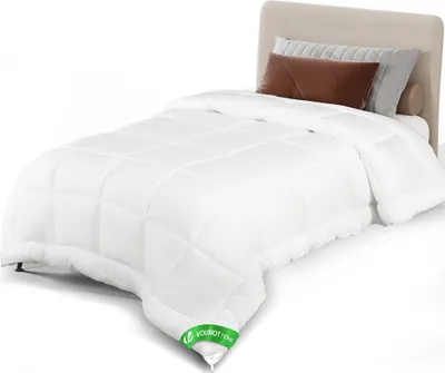 A white comforter is laid out on a bed with a beige headboard and pillows.