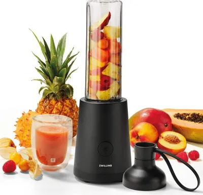 A ZWILLING stand mixer with a glass beaker filled with fruit, surrounded by various fruits and a glass of juice.