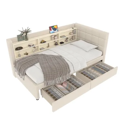A beige upholstered bed with a built-in shelf unit at the headboard and two open drawers underneath, displaying various items. The bed is shown from a slightly elevated, diagonal angle.
