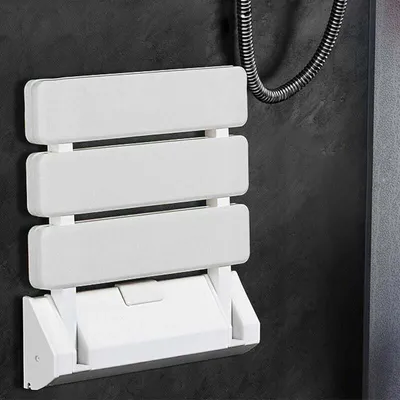 A white foldable shower seat mounted on a dark gray wall.