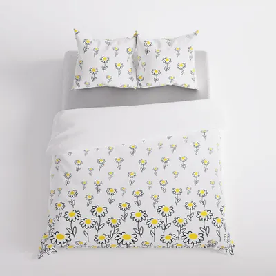 A duvet cover and two pillowcases with a daisy pattern are laid out on a bed.