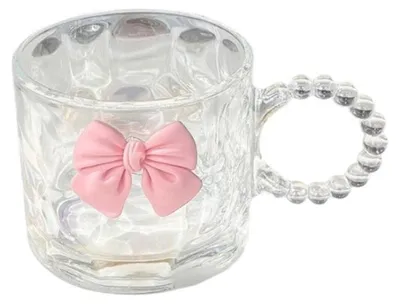 A clear glass mug with a pink bow decoration and a beaded handle, isolated on a white background.