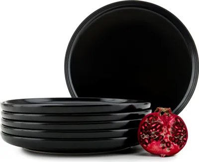 A stack of black plates with a halved pomegranate.