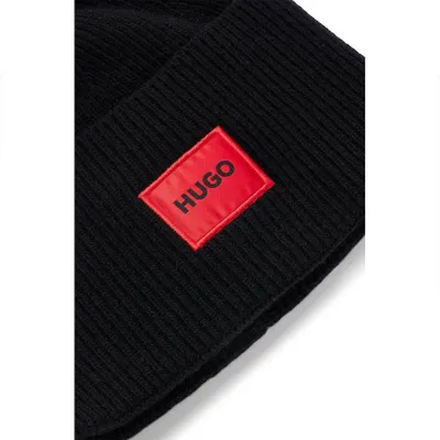 A close-up of a black beanie with a red HUGO logo patch.