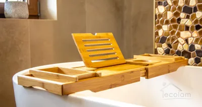 A wooden bathtub tray is placed on the edge of a white bathtub, with a tiled wall in the background.