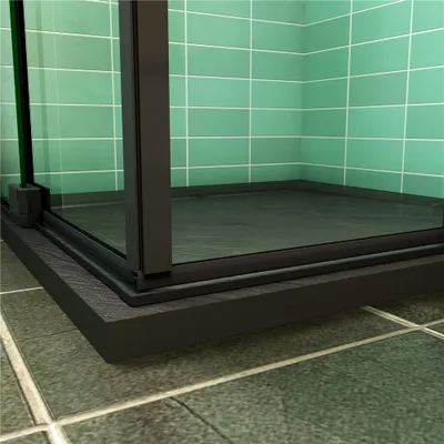 A close-up view of the corner of a shower enclosure with black framing and clear glass panels, set against a background of green tiled walls and a tiled floor.