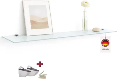 A glass shelf mounted on a white wall, decorated with a framed picture, a vase with a flower, and a stone.