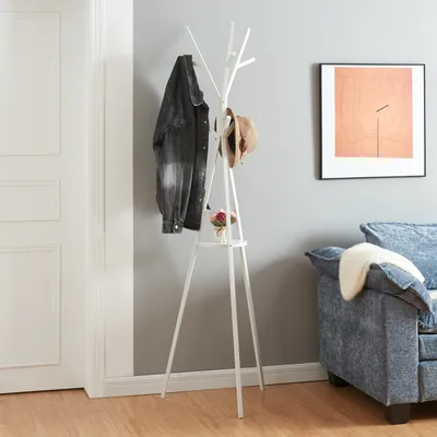 A white coat rack with a jacket and hat on it, placed next to a door and a sofa.