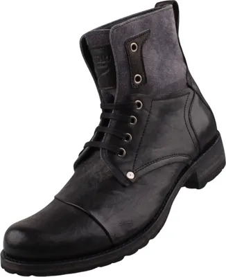 Das Bild zeigt einen schwarzen Stiefel der auf der linken Seite zu sehen ist. Der Stiefel hat eine hohe Form und eine strukturierte Oberfläche.