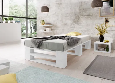 A bedroom scene with a white pallet bed, bedding, and decorative items.