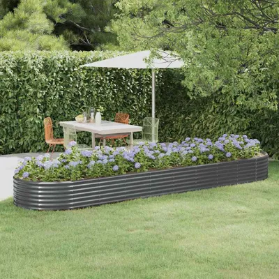 A raised garden bed filled with purple flowers sits in a garden setting with a table and chairs under an umbrella in the background.