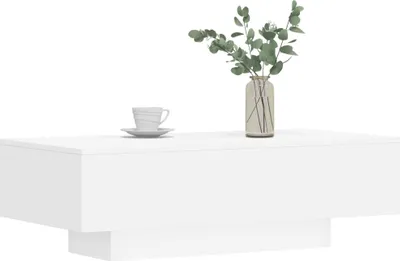 A white coffee table with a vase of greenery and a coffee cup on top.