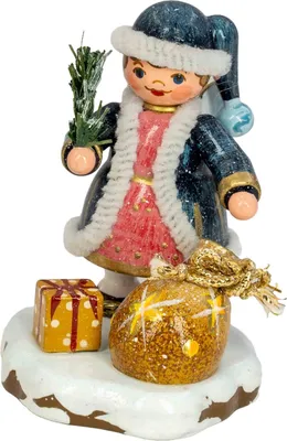 Ein kleines Himmelskind in einem blauen Mantel mit weißem Fellbesatz hält einen Zweig in der Hand und steht auf einer schneebedeckten Basis neben zwei Geschenken die mit goldenen und roten Details verziert sind