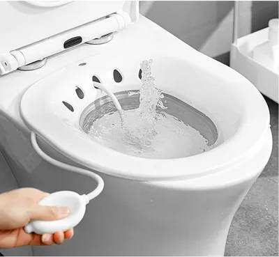 A hand is shown squeezing a bulb to operate a bidet attachment on a toilet.