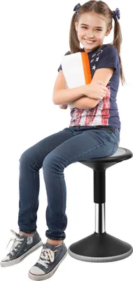A young girl with pigtails sitting on an adjustable stool, holding a book.