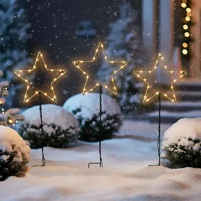 Three illuminated star-shaped garden stakes are placed in the snow, decorated with small lights.