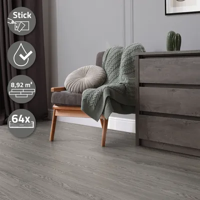 A chair with a blanket and pillow sits on a gray wood-look floor next to a dresser.
