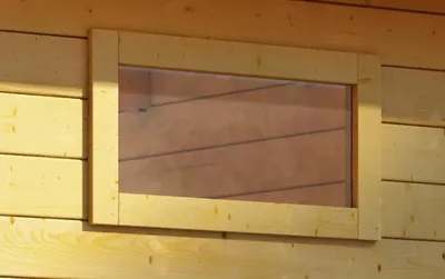 A close-up view of a wooden window frame with a clear pane, installed on a wooden wall.