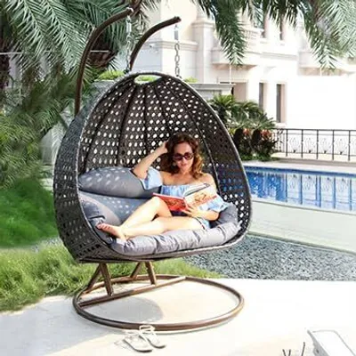 A woman is relaxing in a hanging chair by a pool, reading a book.