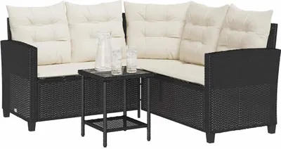 A black poly rattan L-shaped sofa with cream cushions and a small black coffee table with two glasses and a pitcher on it, set against a white background.