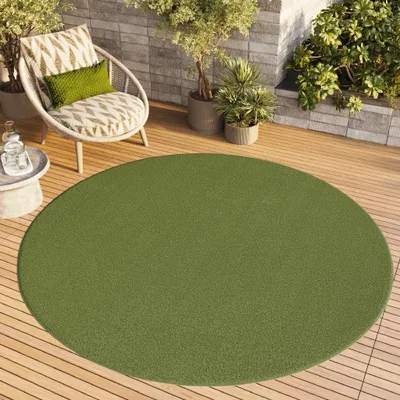 A round green rug on a wooden deck with a chair and plants.