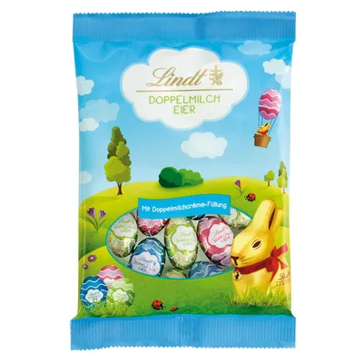 A bag of Lindt chocolate Easter eggs and a chocolate bunny on a grassy, cartoon-like landscape with trees and clouds.