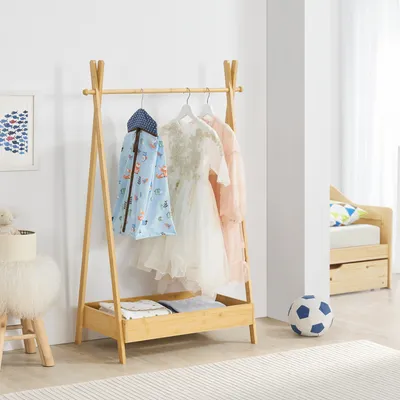 A children's wardrobe stand with clothes hanging on it, placed in a room with a bed and a soccer ball.