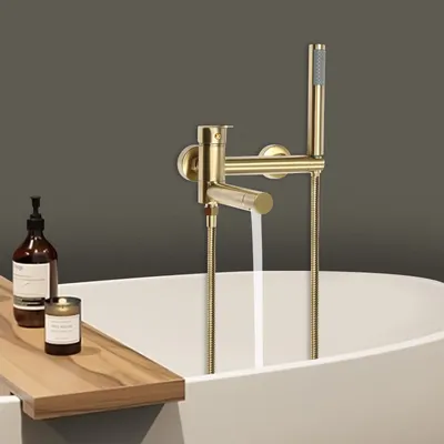 A modern bathroom scene with a gold bathtub faucet and showerhead, a wooden bath tray with a soap dispenser and candle, and a white bathtub.