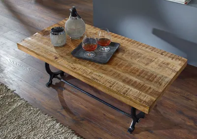 A coffee table with drinks and a decorative bottle on it, placed on a rug and wooden floor.