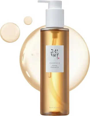 A bottle of cleansing oil with two droplets of oil next to it, set against a soft, blurred background.