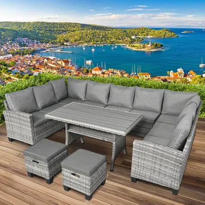A polyrattan garden seating set is placed on a wooden deck with a scenic view of a coastal town and the sea in the background.