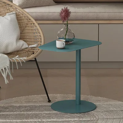A teal side table with a vase and cup on it, next to a wicker chair.
