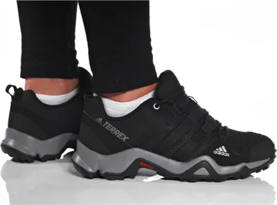 A person wearing black pants and white socks is shown wearing a pair of black Adidas Terrex hiking shoes.