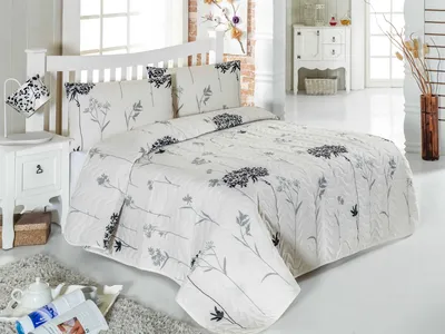 A neatly made bed with a white headboard and a white duvet cover with a floral pattern in gray and black.
