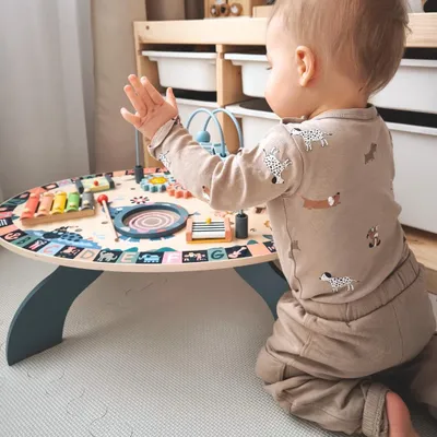 A baby is playing with a colorful wooden activity table.