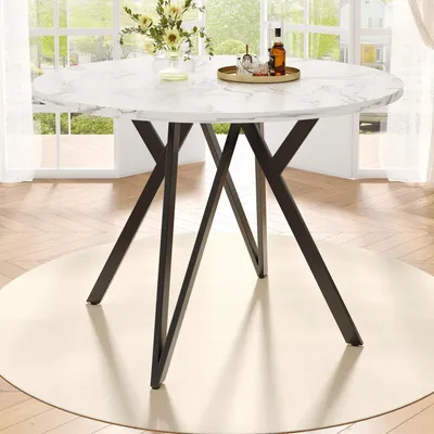 A round dining table with a marble-effect top and black metal legs, set in a bright room with large windows and curtains.