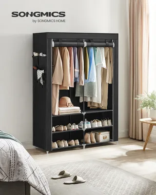 A black fabric wardrobe with clothes and shoes inside, placed in a bedroom setting.