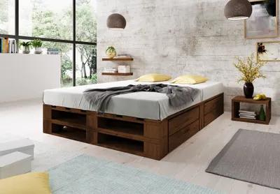 A bedroom scene featuring a wooden pallet bed with storage drawers, bedside table, and decor.