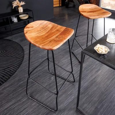 Two wooden bar stools with black metal legs are shown in a modern interior setting, with a black table and a rug visible.