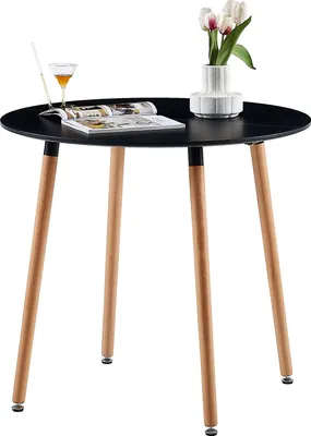 A round black table with three wooden legs, a vase with tulips, and a drink on it.