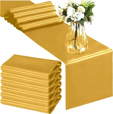 A stack of folded gold satin table runners and a gold satin table runner laid out on a surface with a vase of flowers.