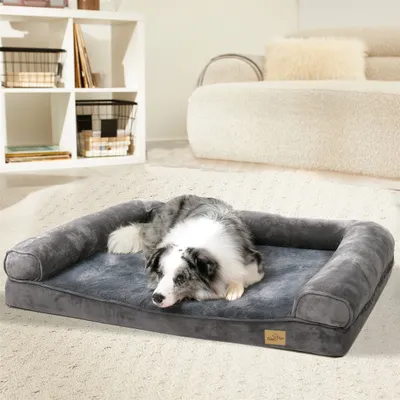 A dog is resting on a gray orthopedic dog bed in a living room setting.