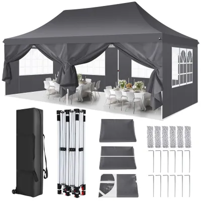 A grey pop-up canopy tent set up with tables and chairs inside, with various components of the tent laid out below.