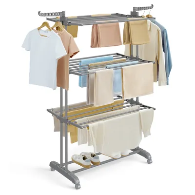A multi-tiered drying rack with various clothing items draped over it, including t-shirts, towels, and pants. A pair of shoes is placed on the bottom shelf.