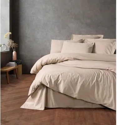 A neatly made bed with beige bedding in a room with a textured gray wall and wooden floor.