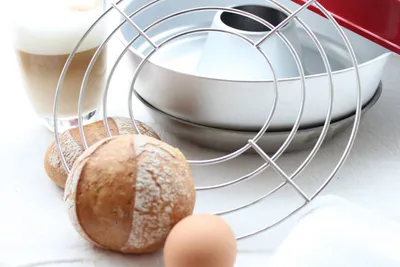 A baking rack with bread rolls, an egg, and a glass of coffee.