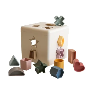 A shape sorter toy cube with various geometric shapes scattered around it.