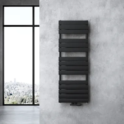 A black radiator is mounted on a concrete wall next to a large window with a view of a snowy landscape.