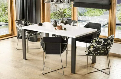 A dining table with chairs in a well-lit room with large windows overlooking a garden.